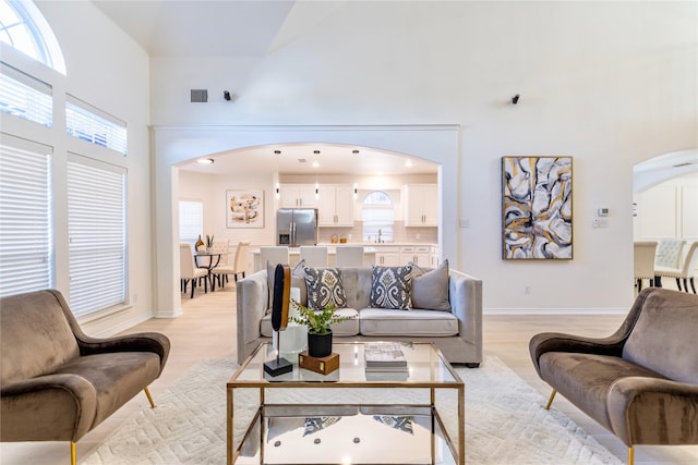 living area featuring arched walkways, a towering ceiling, light wood finished floors, and baseboards