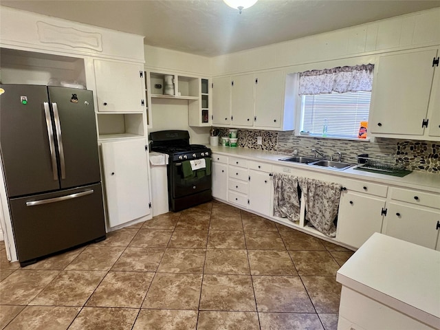 kitchen featuring tile patterned flooring, a sink, black gas stove, freestanding refrigerator, and decorative backsplash