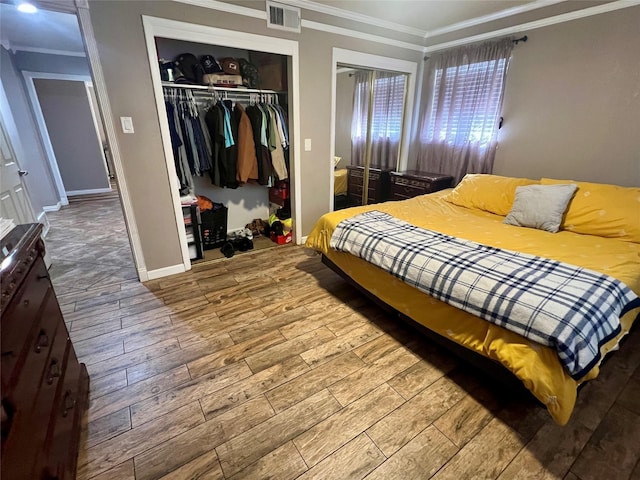 bedroom with wood finished floors, visible vents, baseboards, ornamental molding, and a closet