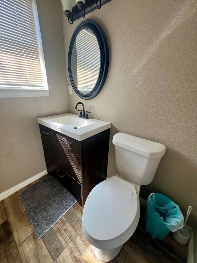 bathroom featuring toilet, baseboards, wood finished floors, and vanity