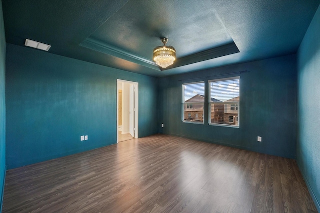 unfurnished room featuring a raised ceiling, visible vents, an inviting chandelier, a textured ceiling, and wood finished floors