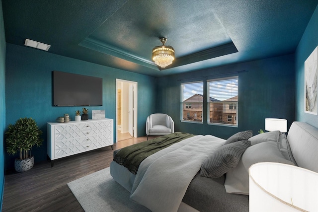 bedroom with an inviting chandelier, a textured ceiling, a raised ceiling, and wood finished floors