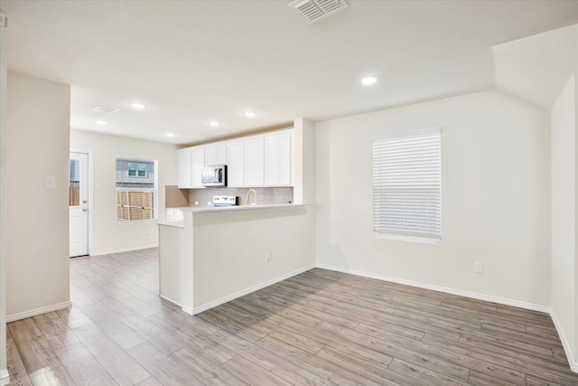 kitchen with visible vents, white cabinets, light wood-style floors, backsplash, and stainless steel microwave