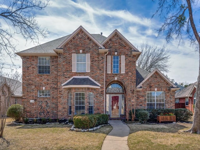 traditional-style home with a shingled roof, brick siding, and a front lawn