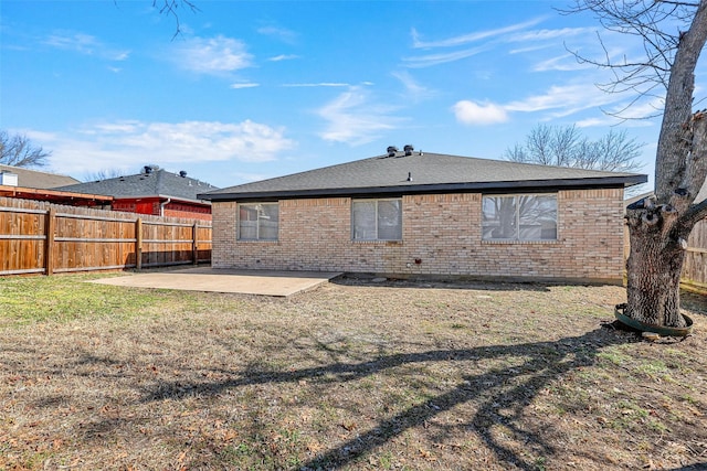 rear view of property with brick siding, a shingled roof, a lawn, a patio area, and a fenced backyard