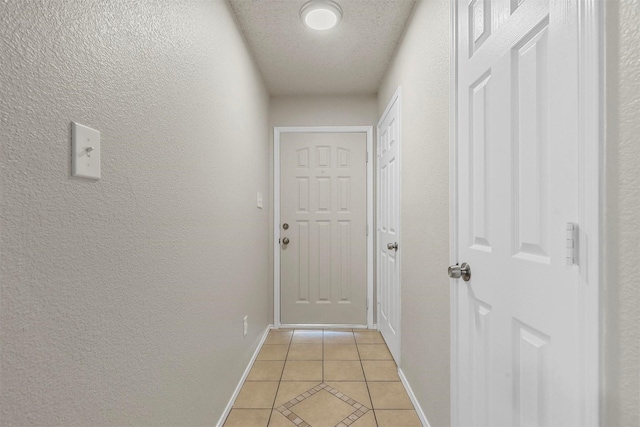 doorway with a textured wall, baseboards, a textured ceiling, and light tile patterned flooring