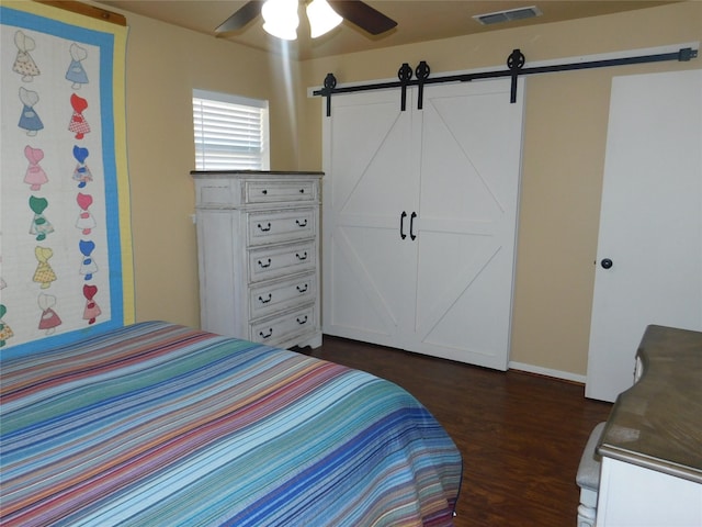 bedroom with dark wood-style floors, visible vents, ceiling fan, and a barn door