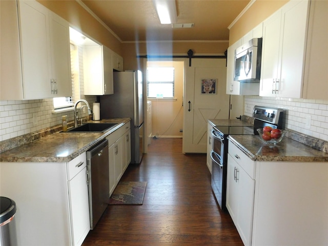 kitchen featuring a barn door, stainless steel appliances, a sink, white cabinetry, and ornamental molding