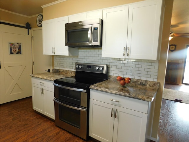 kitchen with crown molding, stainless steel appliances, a barn door, a ceiling fan, and dark wood-type flooring