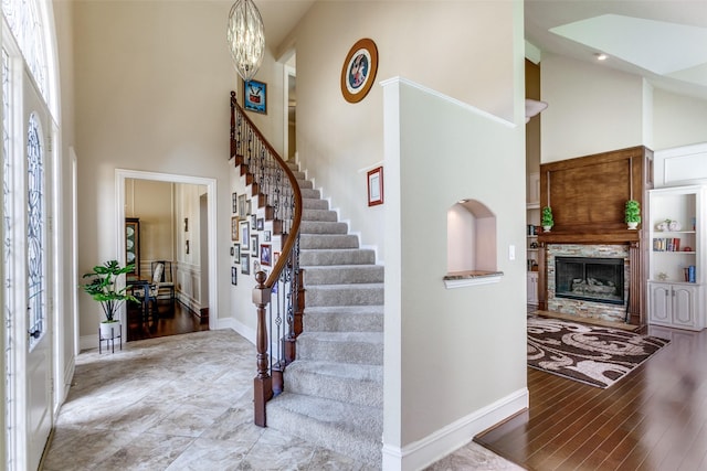 entrance foyer with baseboards, wood finished floors, stairs, a high ceiling, and a fireplace