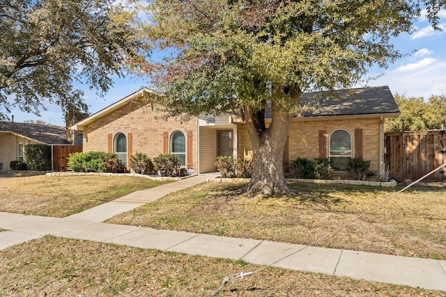 view of front facade featuring brick siding, fence, and a front lawn