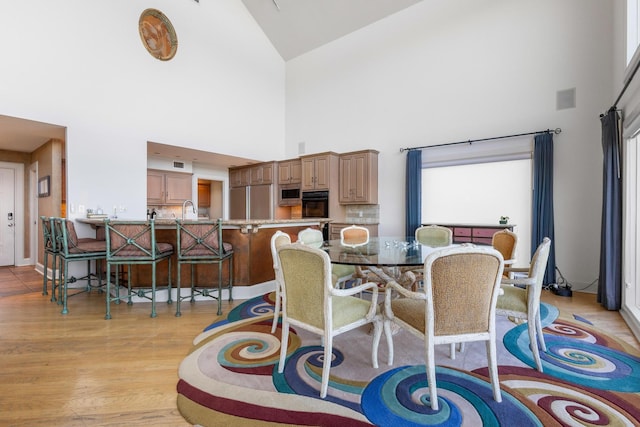 dining room featuring a towering ceiling, light wood-style floors, and visible vents