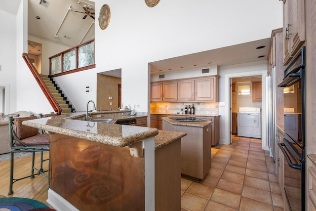 kitchen with a center island, a breakfast bar, visible vents, washer / dryer, and black appliances