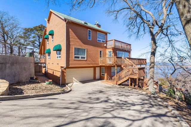 rear view of property featuring an attached garage, driveway, stairs, and a chimney