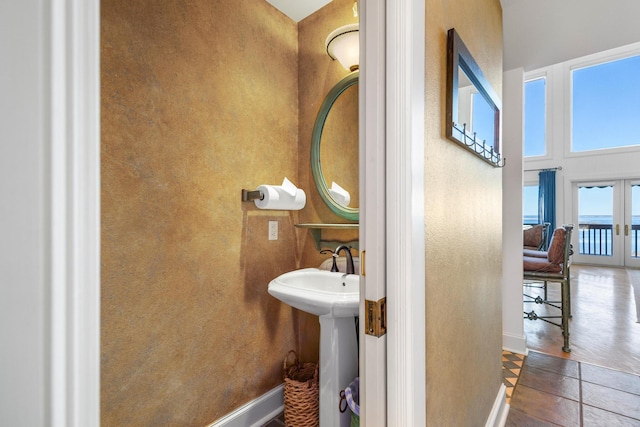 bathroom featuring french doors, a sink, a high ceiling, and baseboards