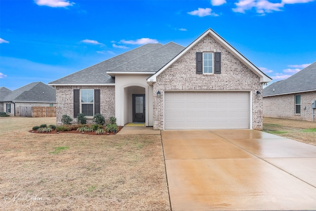 view of front of home with brick siding, a shingled roof, fence, concrete driveway, and a front lawn