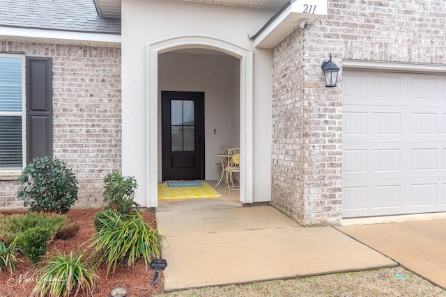 property entrance featuring stucco siding, brick siding, an attached garage, and roof with shingles