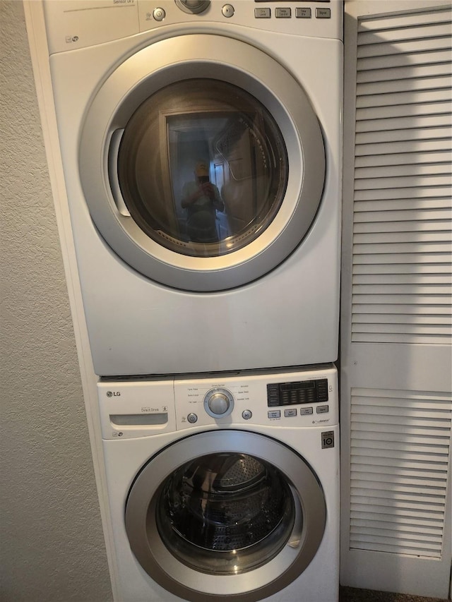 laundry area featuring stacked washing maching and dryer, laundry area, and a textured wall