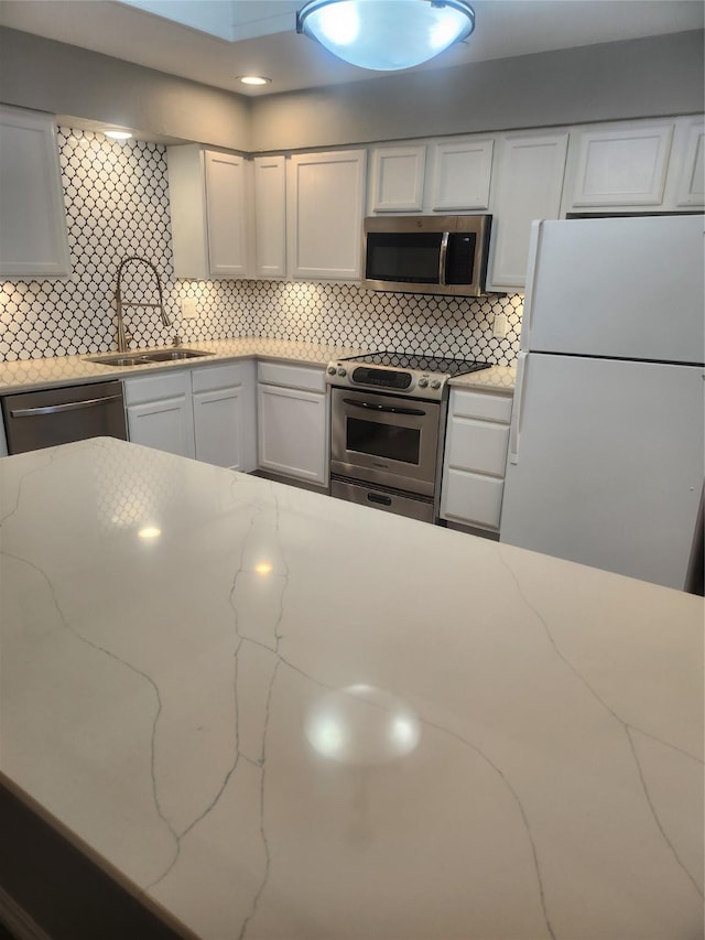 kitchen with appliances with stainless steel finishes, a sink, white cabinets, and decorative backsplash