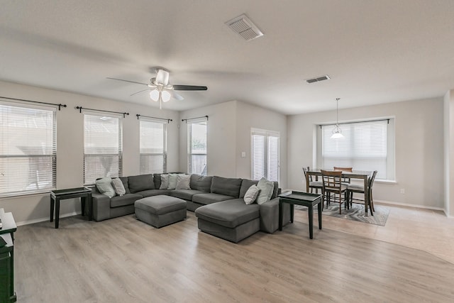 living area featuring light wood-type flooring, baseboards, visible vents, and ceiling fan