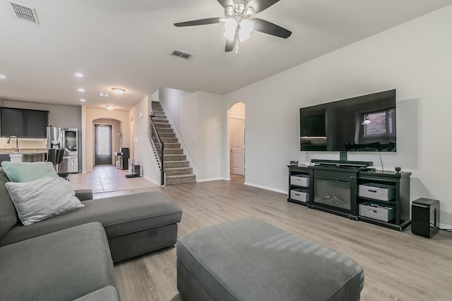 living area featuring stairway, visible vents, arched walkways, and light wood-style floors