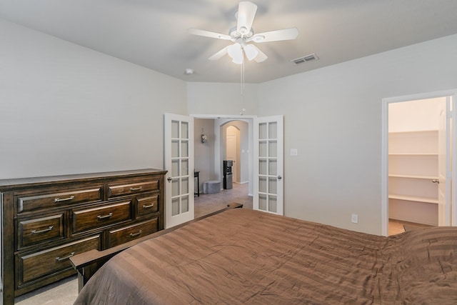 bedroom with visible vents, arched walkways, light colored carpet, a walk in closet, and french doors