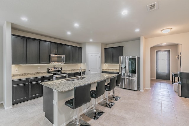 kitchen with arched walkways, stainless steel appliances, visible vents, a sink, and light stone countertops