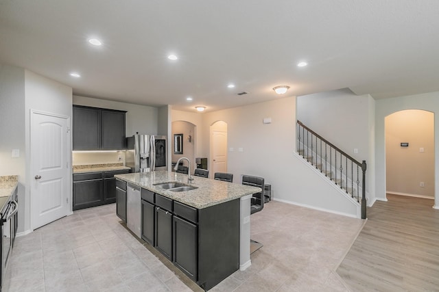 kitchen featuring arched walkways, stainless steel appliances, a sink, and a center island with sink