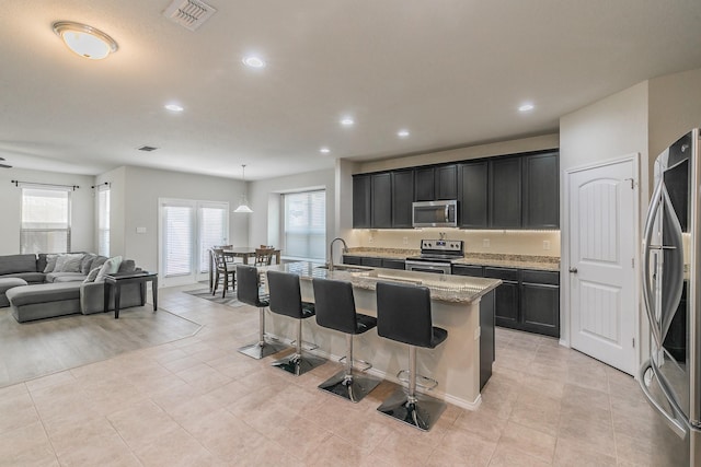 kitchen featuring visible vents, appliances with stainless steel finishes, open floor plan, a sink, and a kitchen breakfast bar