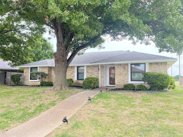 ranch-style house featuring brick siding, a shingled roof, fence, and a front yard