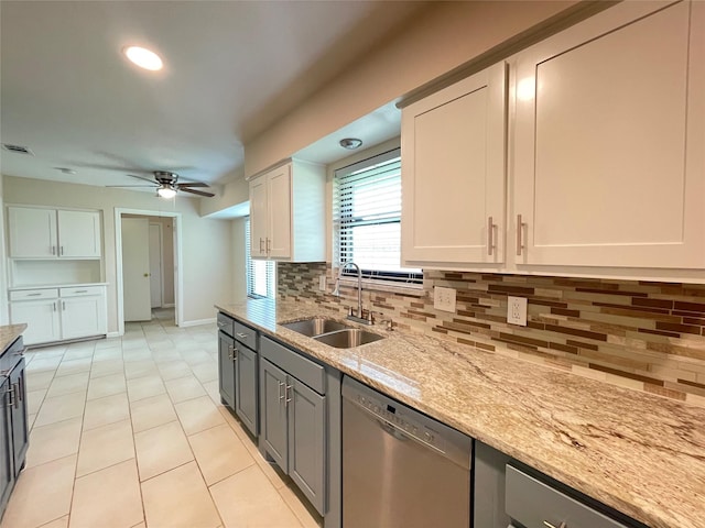 kitchen featuring light stone counters, tasteful backsplash, stainless steel dishwasher, a ceiling fan, and a sink