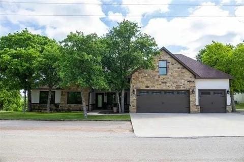 view of front of property featuring an attached garage, stone siding, and concrete driveway