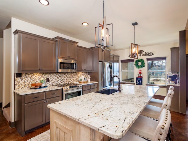 kitchen with stainless steel appliances, light stone counters, an island with sink, and decorative backsplash