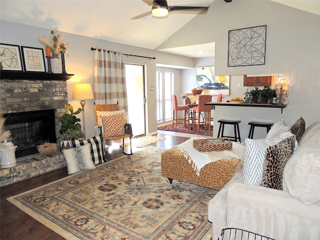 living room featuring vaulted ceiling, ceiling fan, a brick fireplace, and wood finished floors