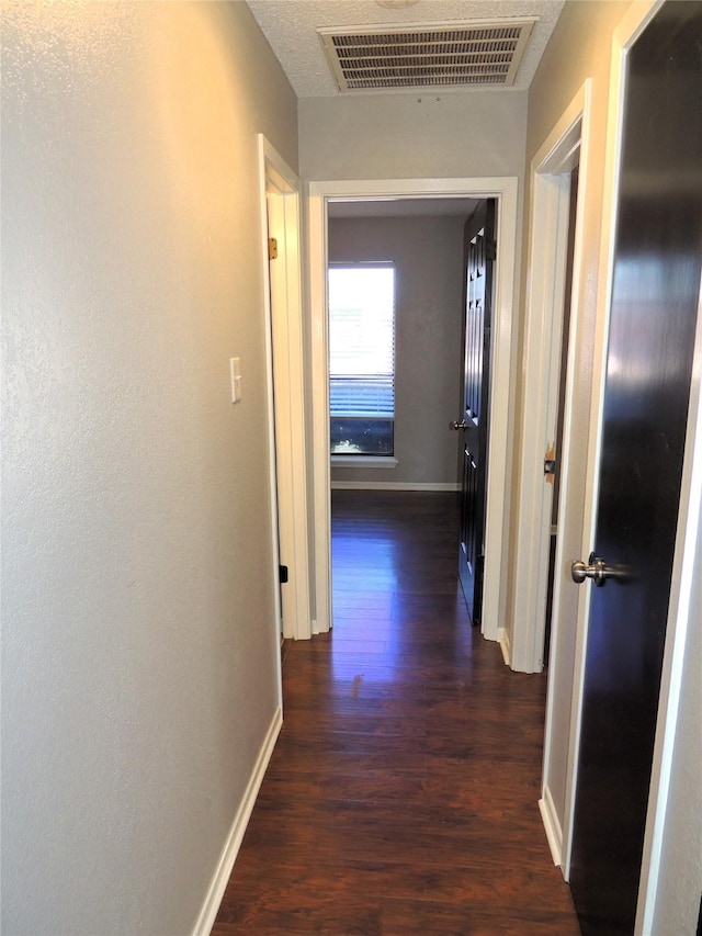 hallway with visible vents, dark wood finished floors, and baseboards