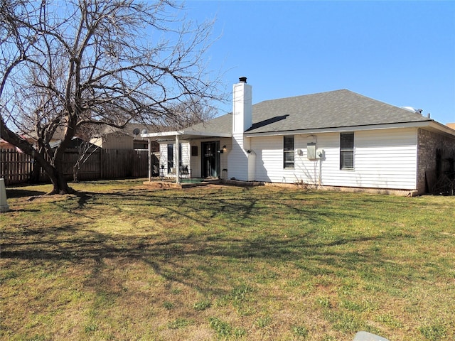 rear view of house with roof with shingles, a chimney, fence, and a yard