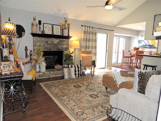 living area featuring lofted ceiling, a fireplace with raised hearth, ceiling fan, and wood finished floors