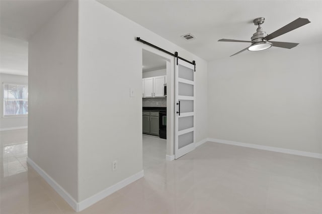 empty room featuring visible vents, ceiling fan, baseboards, and a barn door