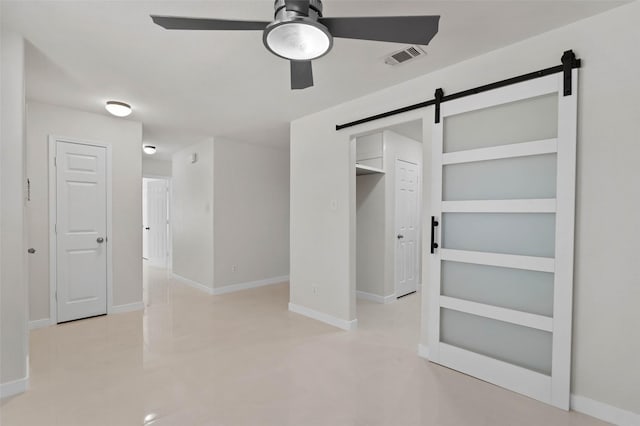 unfurnished bedroom with a barn door, visible vents, ceiling fan, and baseboards