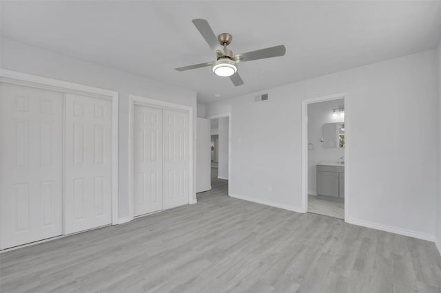 unfurnished bedroom with multiple closets, visible vents, connected bathroom, light wood-type flooring, and baseboards