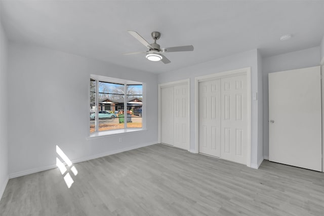 unfurnished bedroom with a ceiling fan, baseboards, two closets, and wood finished floors