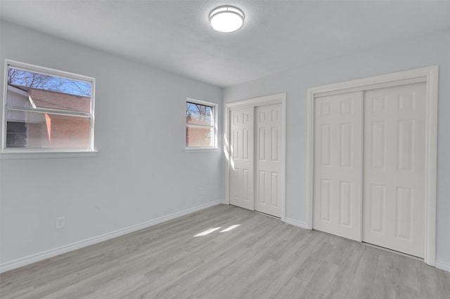 unfurnished bedroom with wood finished floors, baseboards, and two closets