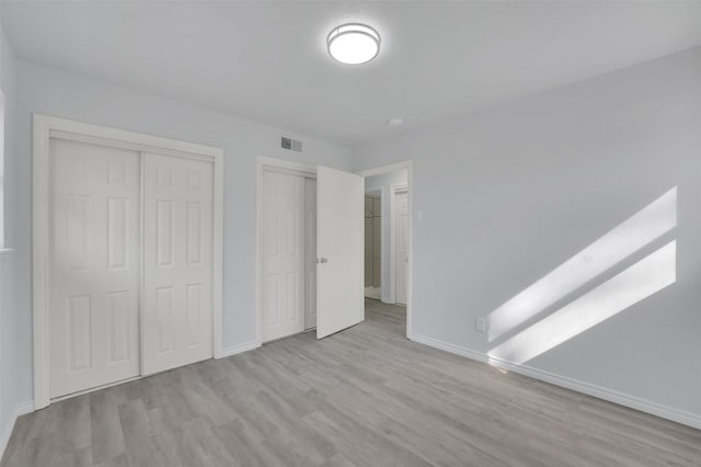 unfurnished bedroom featuring two closets, baseboards, visible vents, and wood finished floors