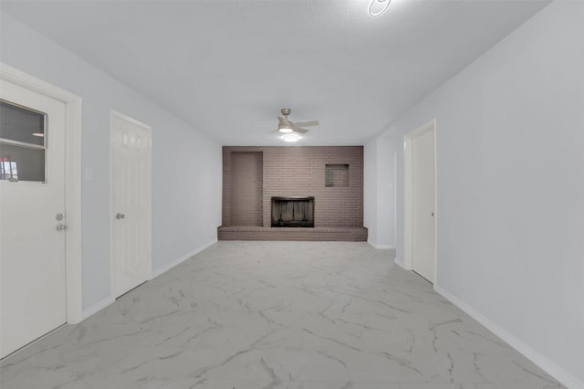 unfurnished living room featuring ceiling fan, a textured ceiling, baseboards, marble finish floor, and a brick fireplace