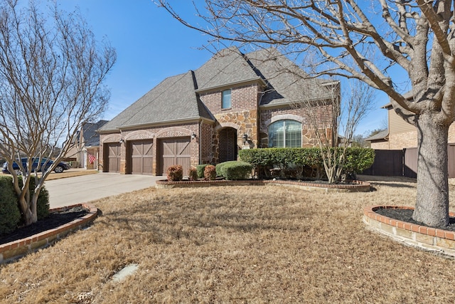 french provincial home with brick siding, roof with shingles, a garage, stone siding, and driveway