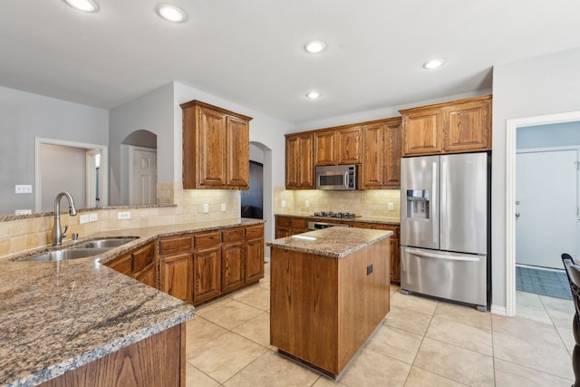 kitchen featuring stone countertops, arched walkways, a sink, appliances with stainless steel finishes, and brown cabinets