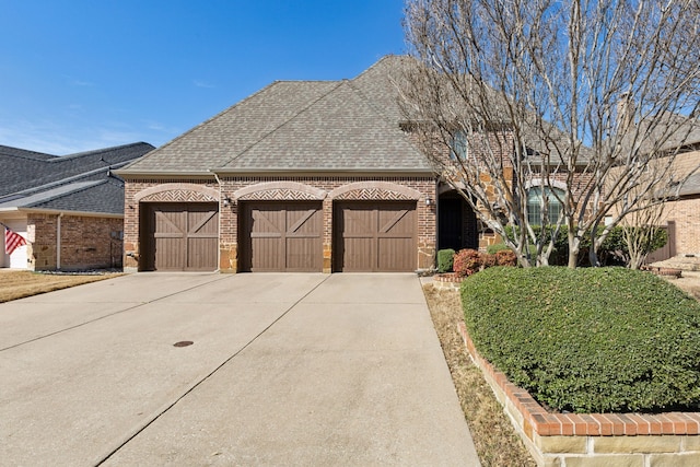 french provincial home featuring a garage, brick siding, concrete driveway, and a shingled roof