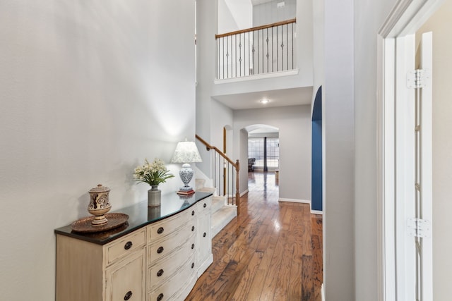 interior space with baseboards, stairway, dark wood-style floors, a high ceiling, and arched walkways