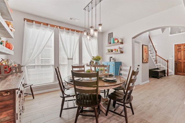 dining space featuring arched walkways, stairway, light wood-type flooring, and visible vents