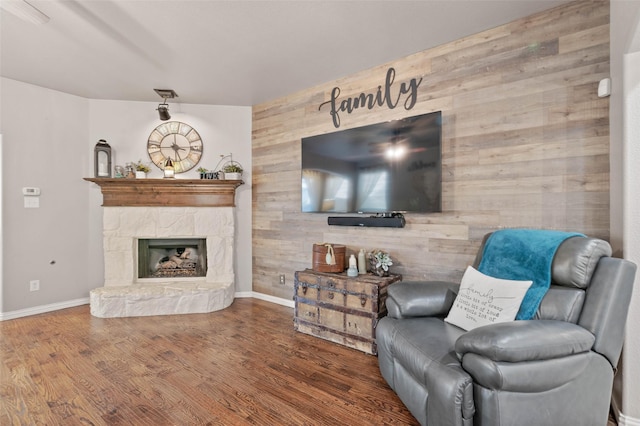 living area with wooden walls, baseboards, wood finished floors, and a stone fireplace